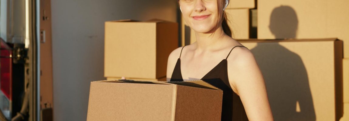 Smiling movers in uniform pose with boxes beside a moving truck.