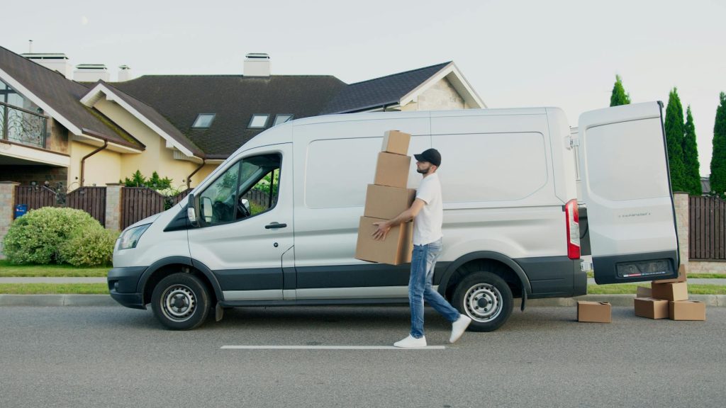 A moving truck parked outside a house with team members carrying a large box.