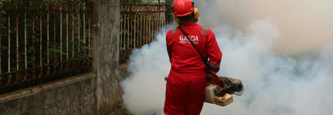 A termite treatment specialist in Nairobi sprays pesticide into the ground near a building's foundation.