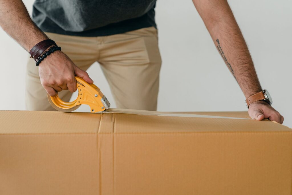 A man in a blue t-shirt lifts a heavy cardboard box inside a moving truck.