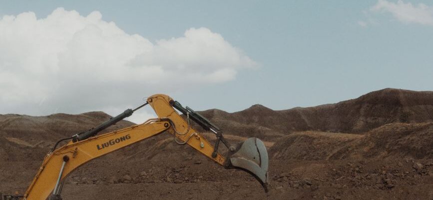 Movers carrying boxes outside homes along a dirt road in Syokimau, near a quarry; call for moving services.