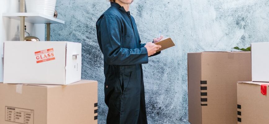 Two movers in matching uniforms carry a large box through a bright, clean doorway inside a building in Kenya.