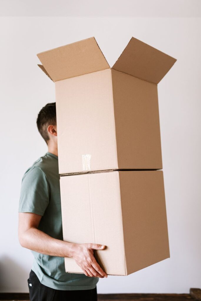 house moving services Kitengela - Two professional movers carrying a large box outside a home in Kitengela, Kenya.