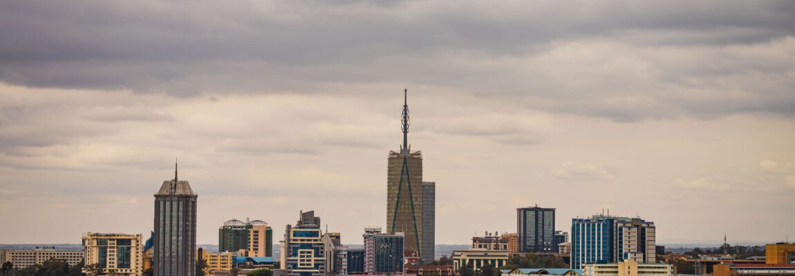Giraffe walking across a road in Nairobi with city buildings in the background.
